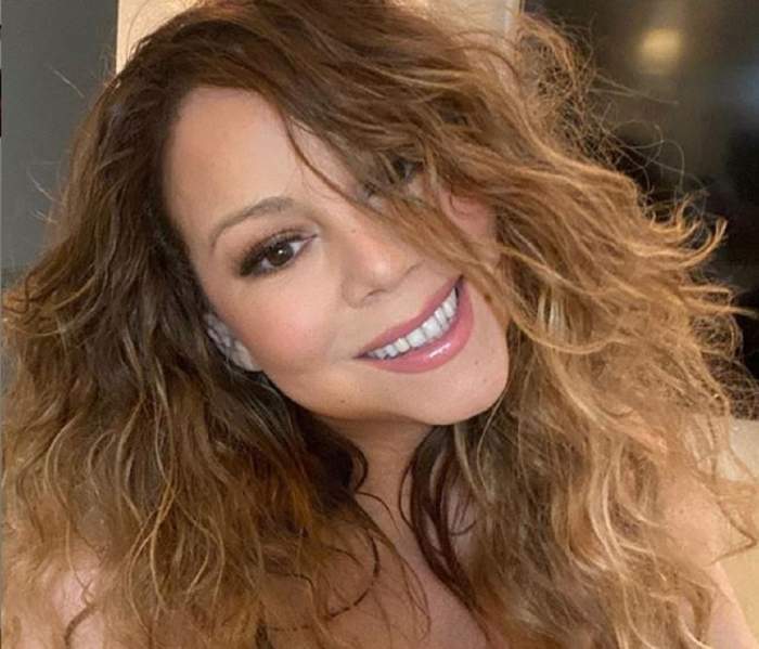 Mariah Carey are părul creț, zâmbind pentru fotografie