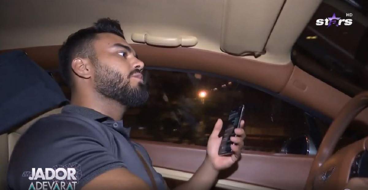 Jador își conduce mașina. Artistul are în mână telefonul mobil și este îmbrăcat într-un tricou albastru.