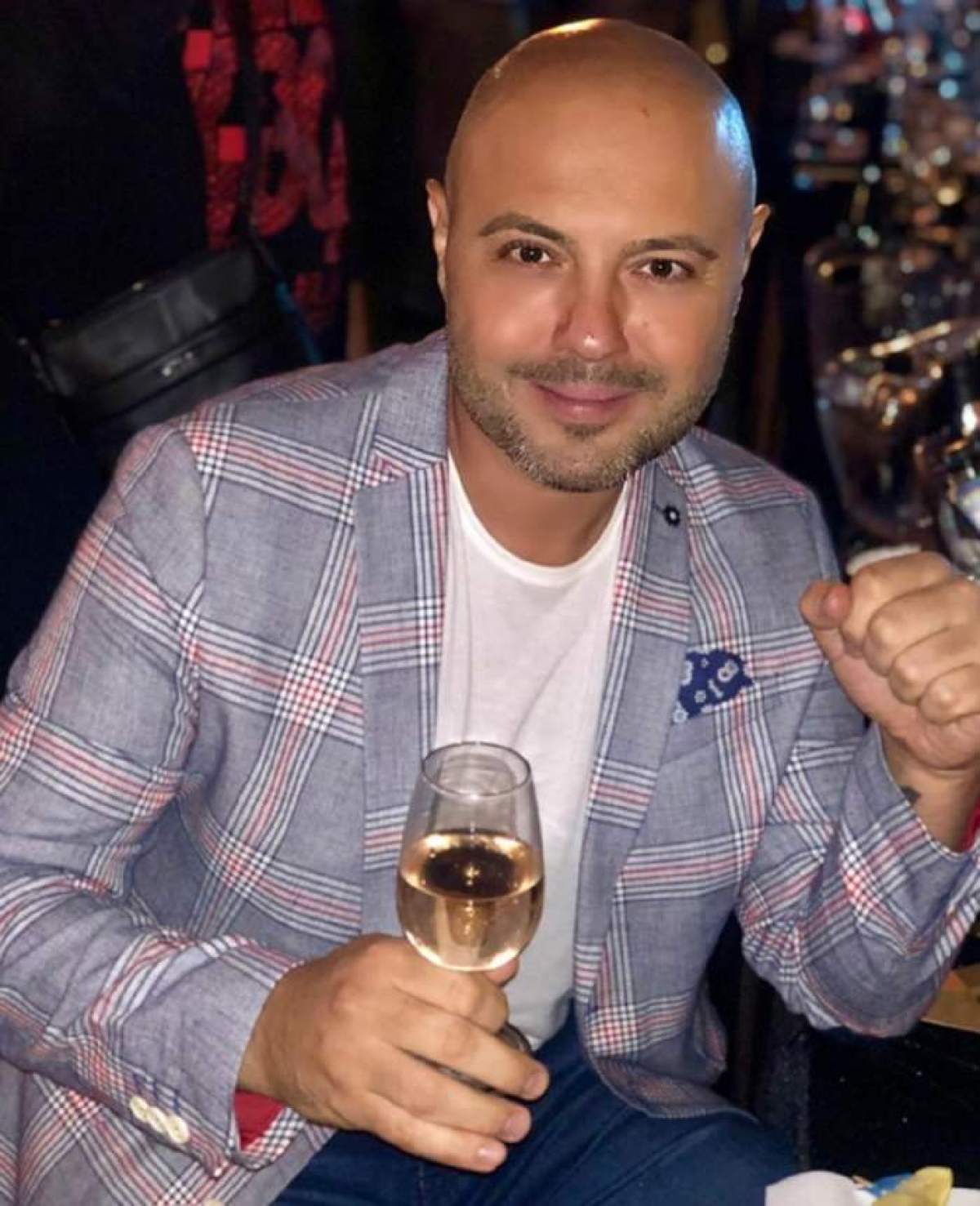 Mihai Mitoșeru, purtând un tricou alb și un sacou mov, se afla la o petrecere, zâmbitor, ținând un pahar cu vin în mână