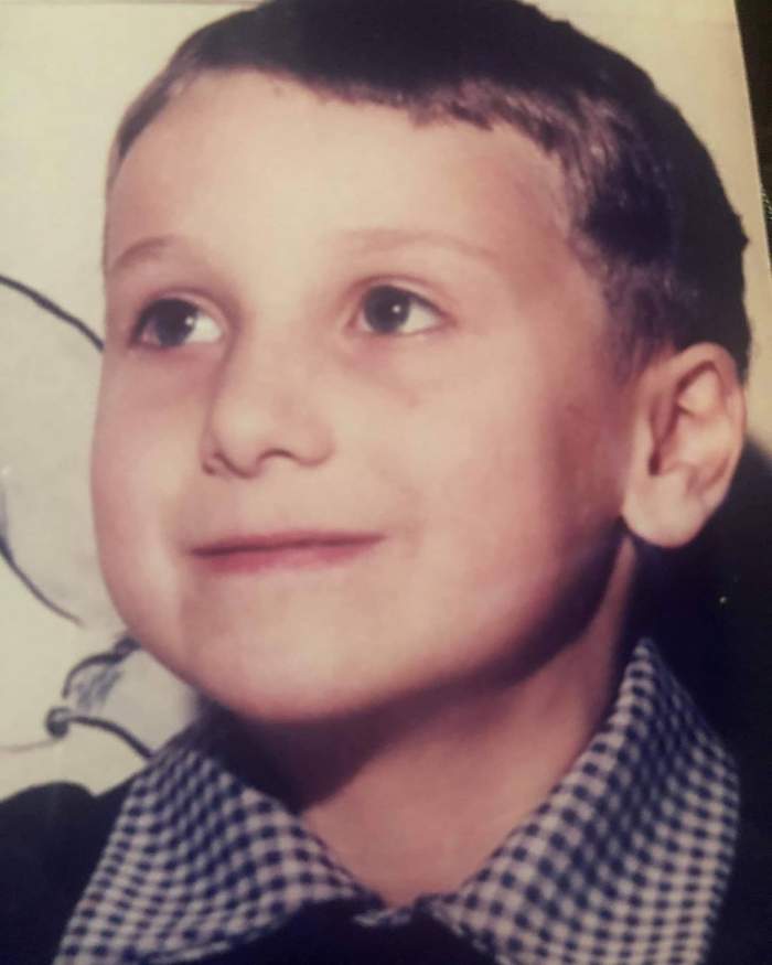 Dani Oțil fotografiat în copilărie, în prima zi de școală, schițând un zâmbet timid