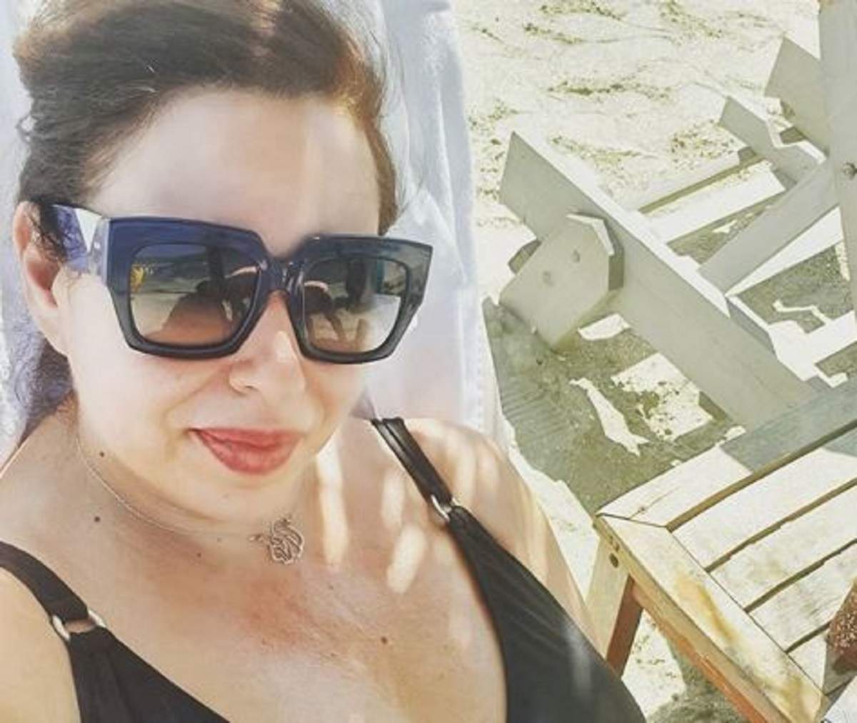 Oana Roman într-un costum de baie negru. Vedeta are părul prins în coadă și poartă ochelari de soare.