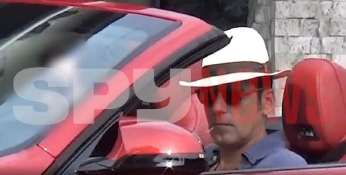 Ștefan Bănică Jr. este la volanul unei mașini roșii. Cântărețul are o scobitoare în gură și o pălărie pe cap.
