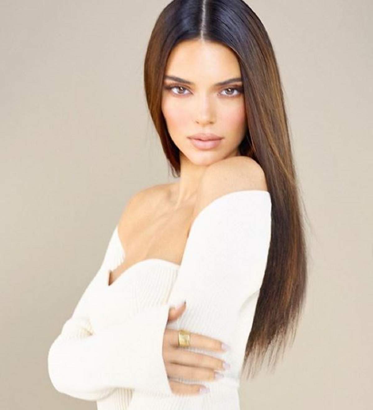 Kendall Jenner într-un shooting foto, modelul poartă o bluză albă fără umeri și are părul desprins, ăși ține brațele strânse