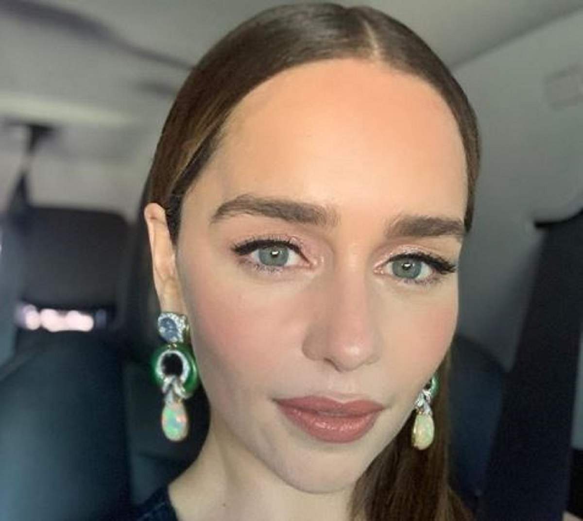 Emilia Clarke în mașină. Artista esta machiată și poartă niște cercei cu perle.