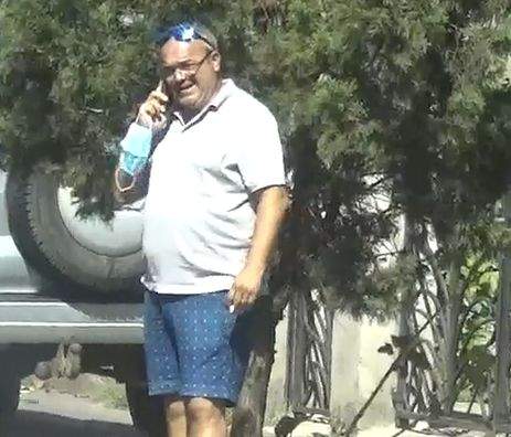 Fiul lui Alexandru Arșinel, îmrăcat într-un tricou alb și pantaloni albaștri, fumează în fața casei