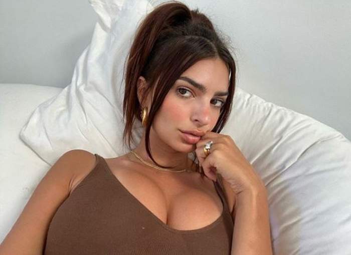 Emily Ratajkowski în pat. Modelul e îmbrăcat cu un maieu maro.