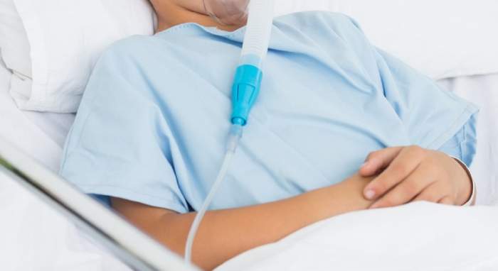 Copil pe patul de spital, conectat la o mască cu oxigen