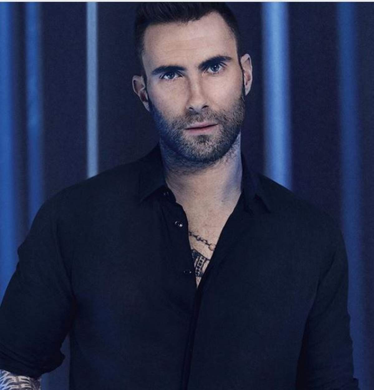 Adam Levine poartă o cămașă neagră și se uită serios la cameră