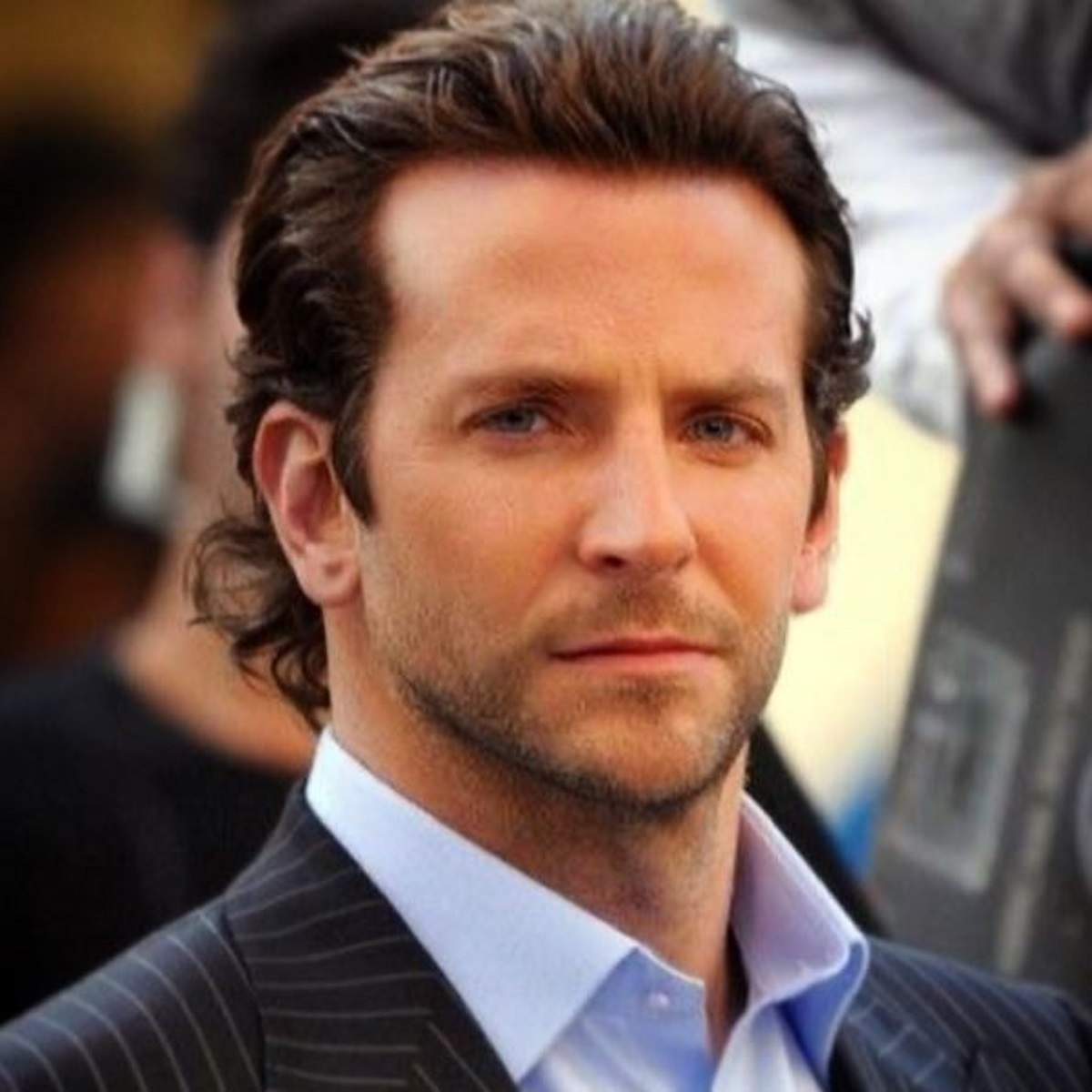 Bradley Cooper îmbrăcat la costum, pozează serios în fața camerei