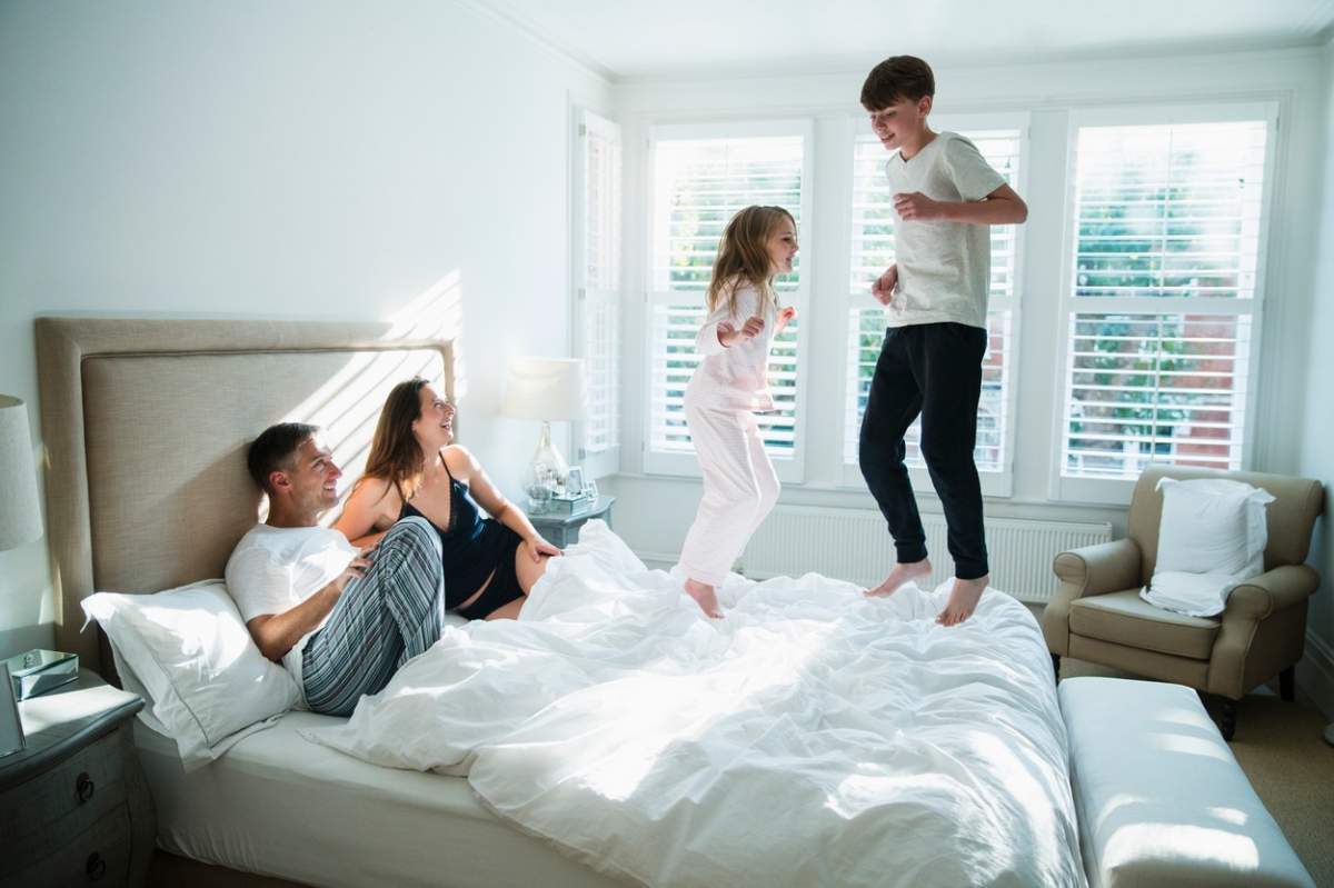 Părinți fericiți se uită cum copiii lor sar pe pat