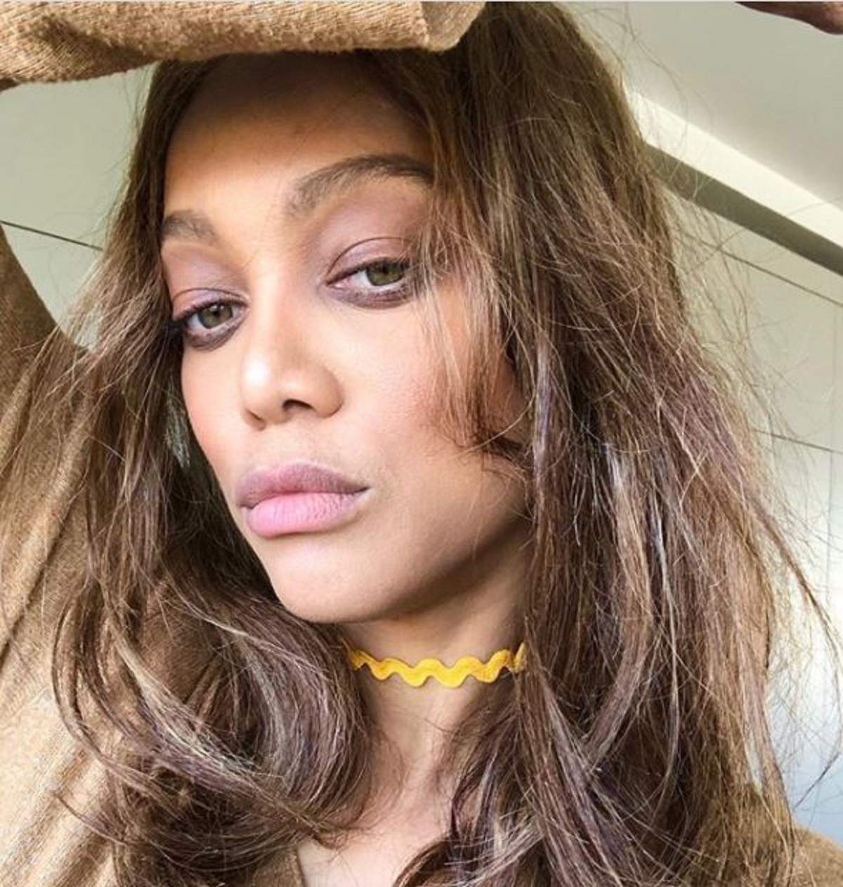 Tyra Banks intr-un selfie in care nu zâmbeste, are părul desprins, este machiată natural și isi tine mana lipita de frunte