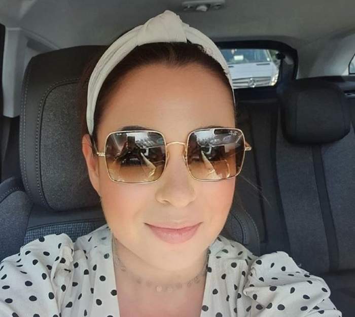 Oana Roman în mașină. Vedeta poartă o bluză albă cu buline negre, ochelari de soare și un turban alb