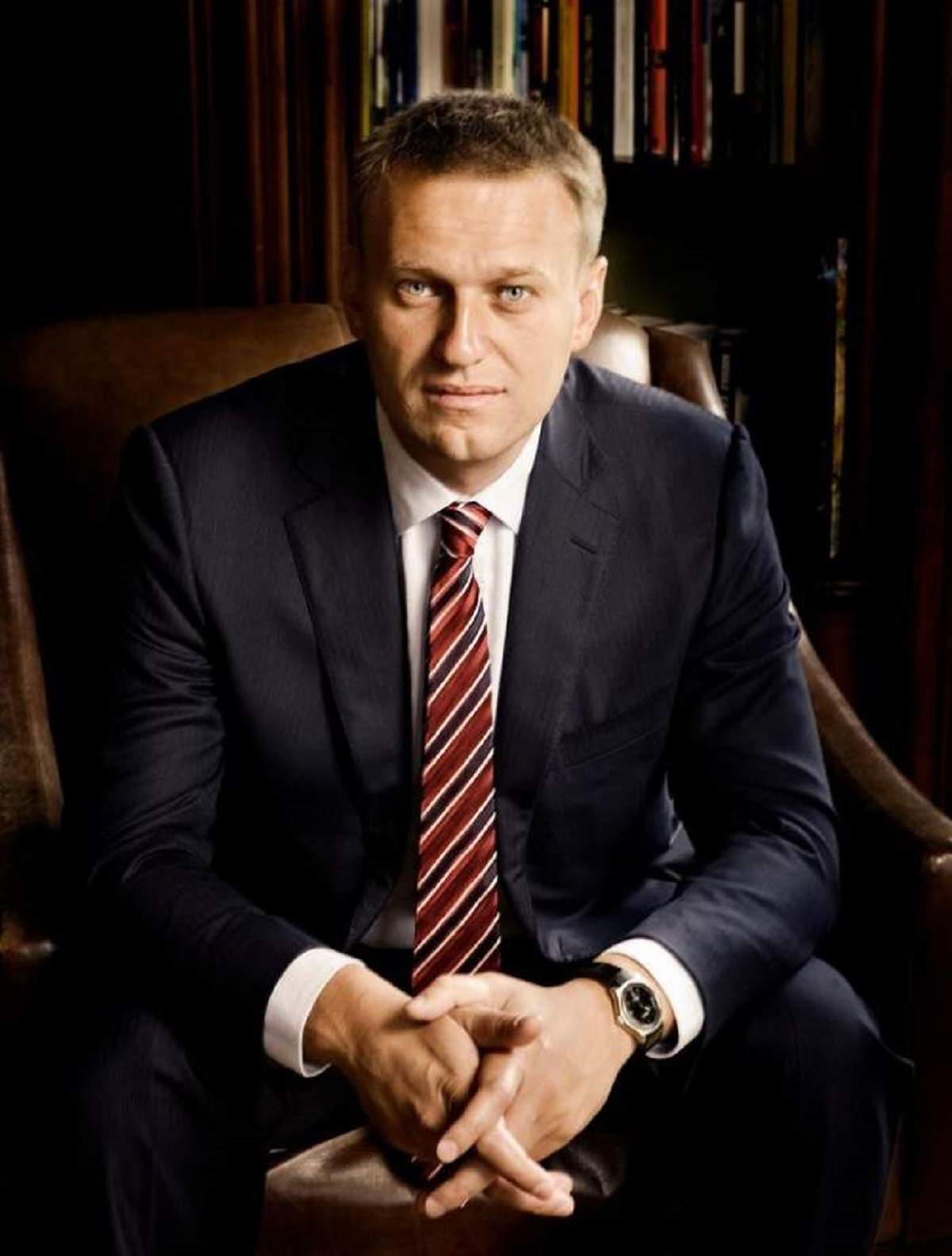 Aleksei Navalnii sta pe scaun, aplecat in fata, poarta costum negru si cravata grena