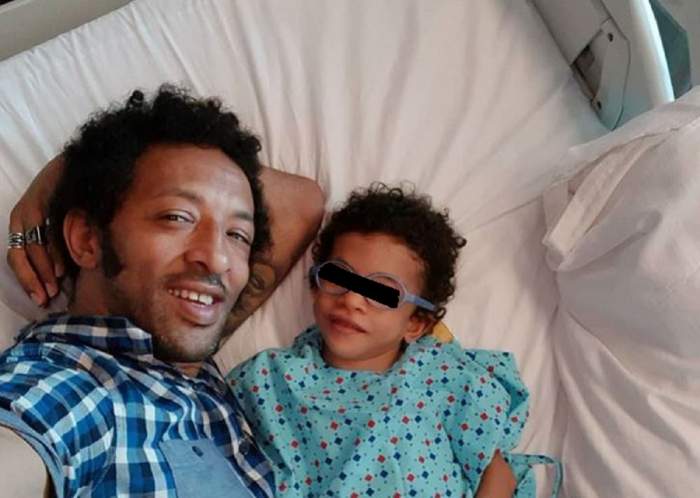 Kamara și fiul lui stau pe un pat de spital. Cei doi zâmbesc larg