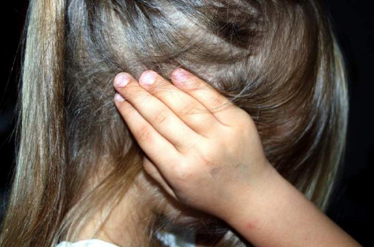 Imagine ilustrativă cu o fetiță atacată, cu mâinile la urechi