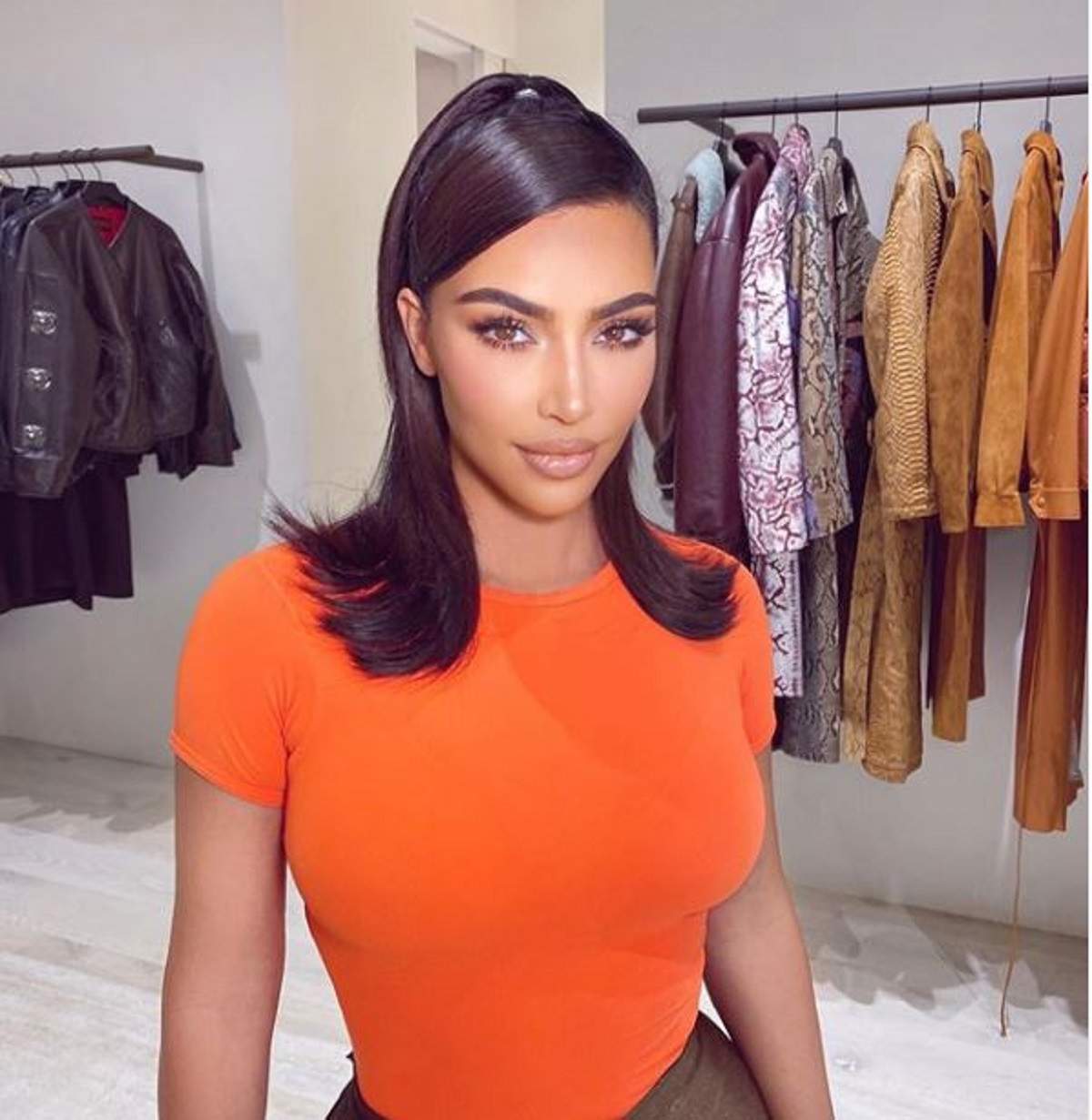 Kim Kardashian este in dressingul ei, poarta un tricou portocaliu si parul prins