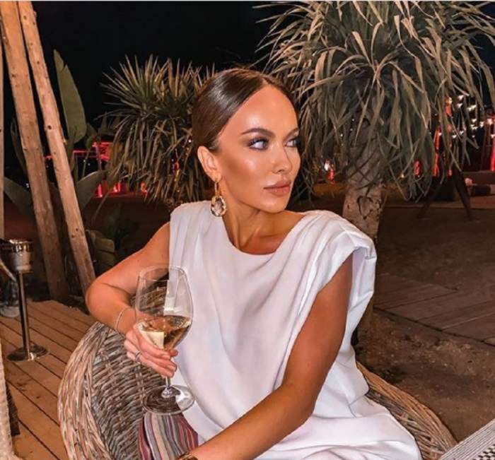 Monica Orlanda la o terasă, poartă o bluză albă și bea vin