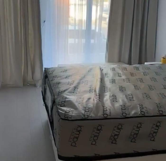 Dormitorul din apartamentul Carminei. Se vede un pat mare, cu saltea albă