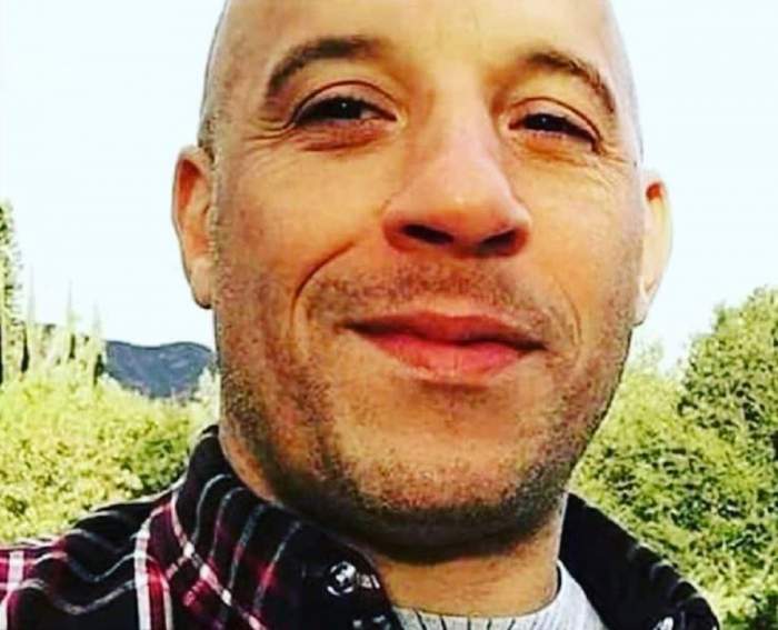 Vin Diesel oiarta o camasa inchisa in carouri si tricou alb, zambeste timid