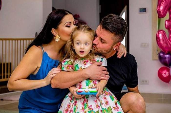 Gabriela Cristea și Tavi Clonda o sărută pe obraji pe fiica lor cea mare, Victoria. Artistul poartă un tricou negru, iar soția lui o rochie albastră.