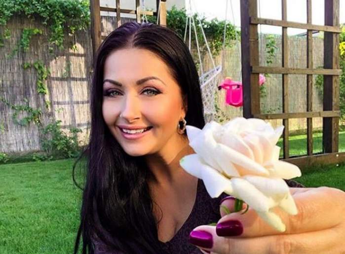 Gabriela Cristea este în curtea casei sale. Vedeta are în mână o floare și zâmbește.