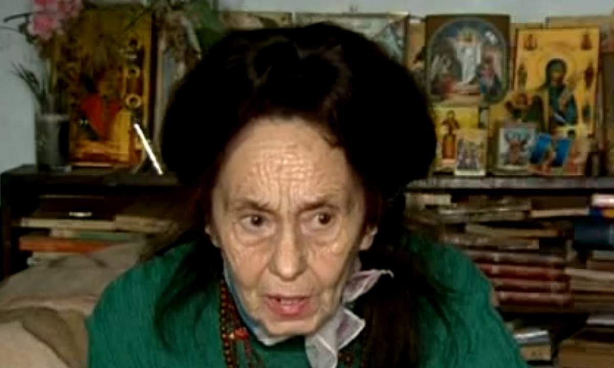 Adriana Iliescu, îmbrăcată în verde, în locuința ei, înconjurată de icoane