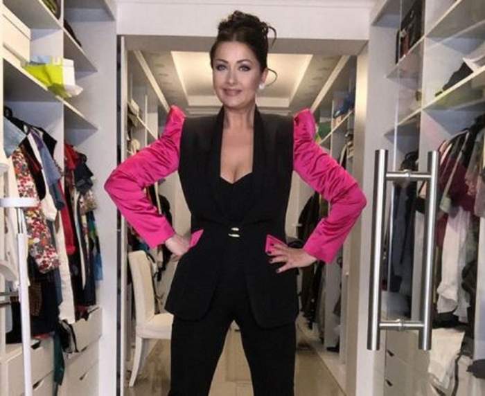 Gabriela Cristea se află în dressing-ul său. Vedeta poartă un costum negru, cu umeri roz și are părul prins în coc.