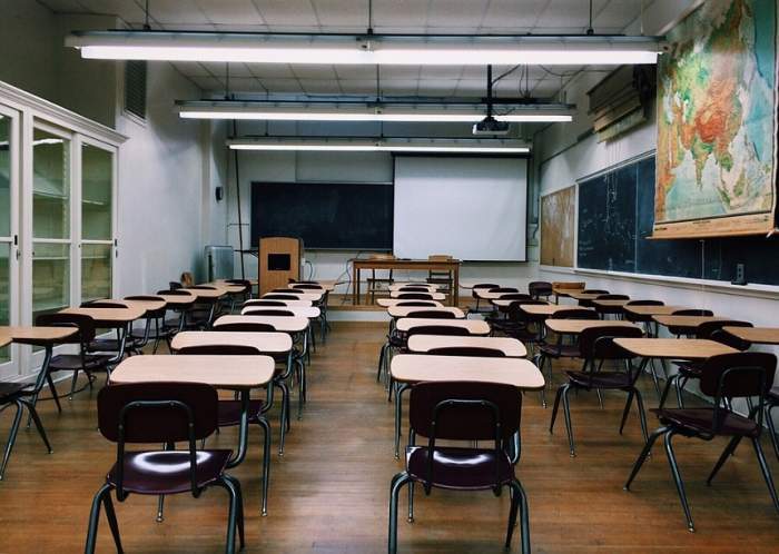 Fotografie cu o sala de curs goală, doar cu mese, scaune și hărți agătate pe pereți