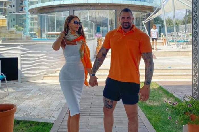 Bianca Drăgușanu și Alex Bodi se țin de mână. Afaceristul poartă un tricou portocaliu și pantaloni scurți, negri. Blondina e îmbrăcată în rochie albă.