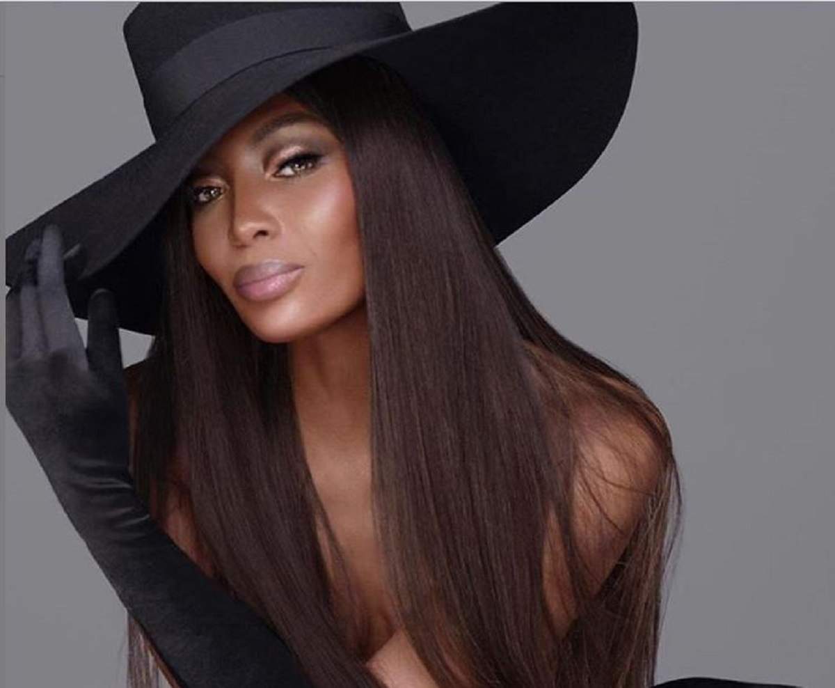 Naomi Campbell este la o ședință foto și poartă o pălărie de dimensiuni mari, neagră și mănuși negre