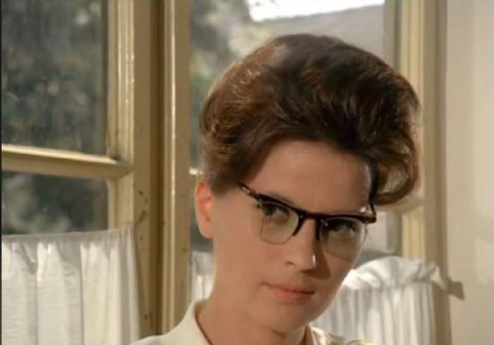 Doamna profesoară de istorie din filmul „Pistruiatul”, poartă ochelari și are părul prins