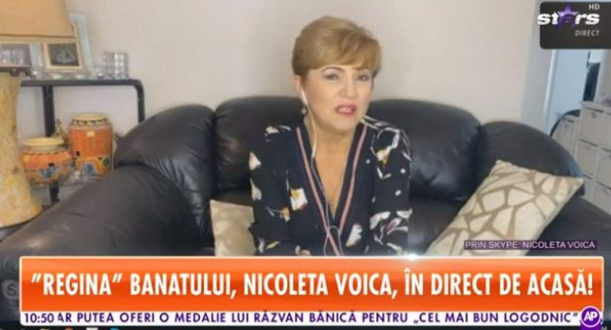 Nicoleta Voica, îmbrăcată în negru cu flori, așezată pe un fotoliu negru din propria casă