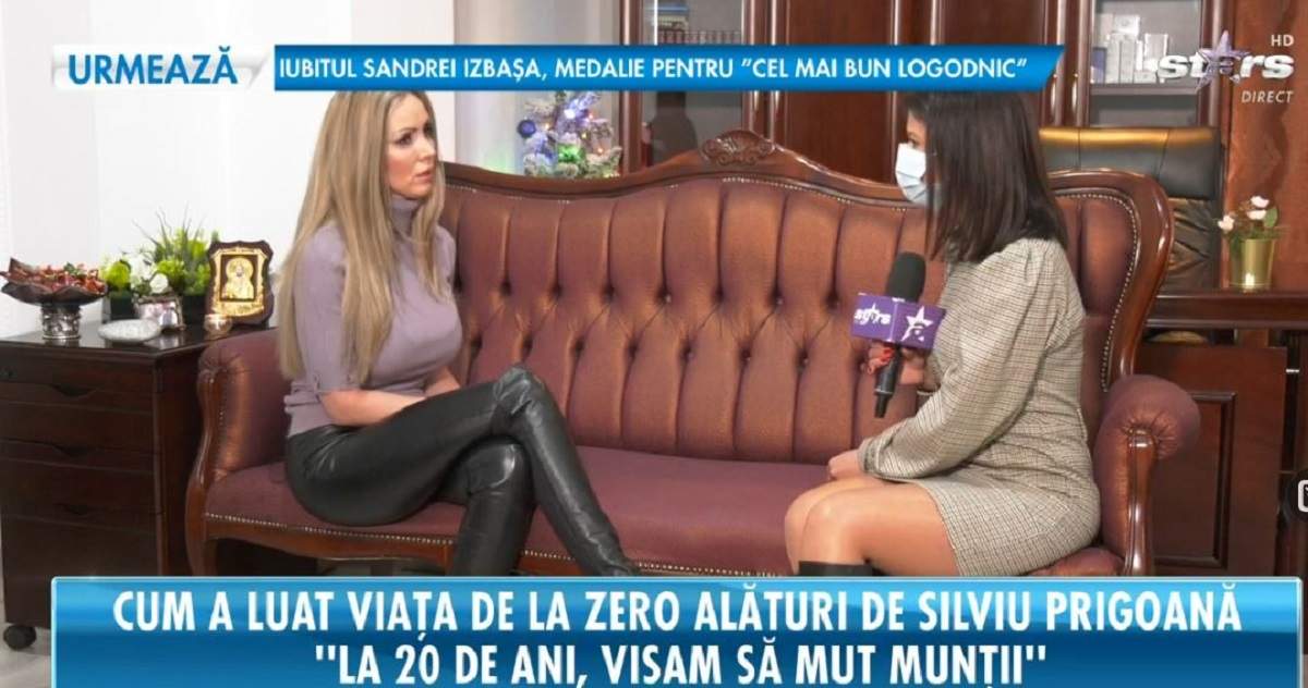Mihaela Prigoană stă pe canapea și dă un interviu pentru Antena Stars. Vedeta poartă o bluză gri și nișe pantaloni din piele, negri.