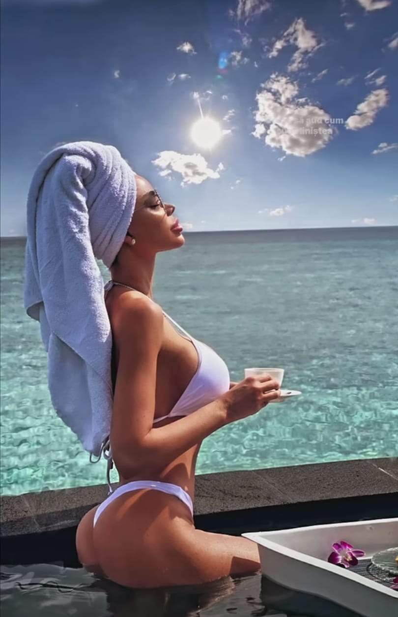 Bianca Drăgușanu, în costum de baie alb, cu prosop alb pe cap, la marginea piscinei, cu o cană de cafea în mână