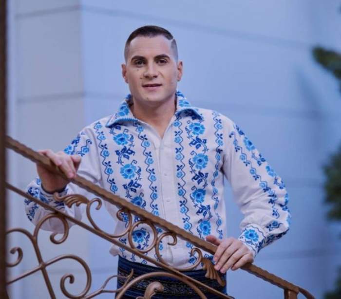 Mihai Priescu, în pantaloni negri și cămașă alb-albastră, cu motive tradiționale, în spatele unei balustrade