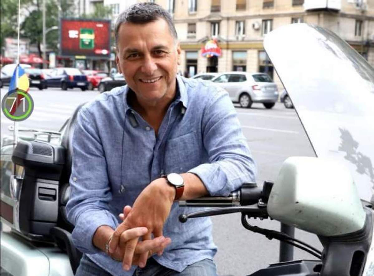 Bogdan Stanoevici, zâmbitor, așezat pe motocicleta lui, în cămașă albastră
