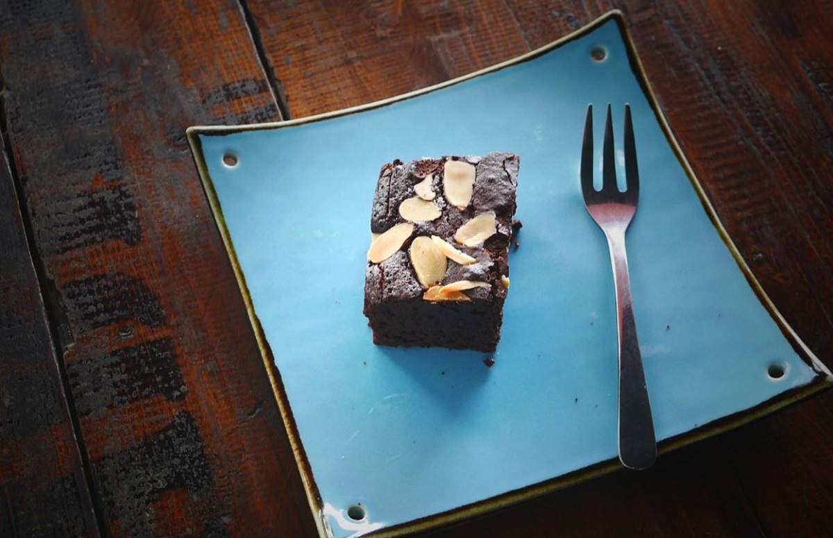 O bucată de prăjitură negresă așezată pe o farfurie albastră. Lângă ea este o furculiță.