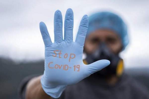 Mâna unui medic, cu mănușă, pe care scrie ”stop COVID-19”