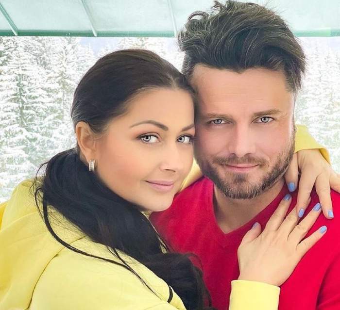 Gabriela Cristea și Tavi Clonda se țin în brațe. Ea poartă un hanorac galben și are părul prins în coadă, iar el o bluză roșie.