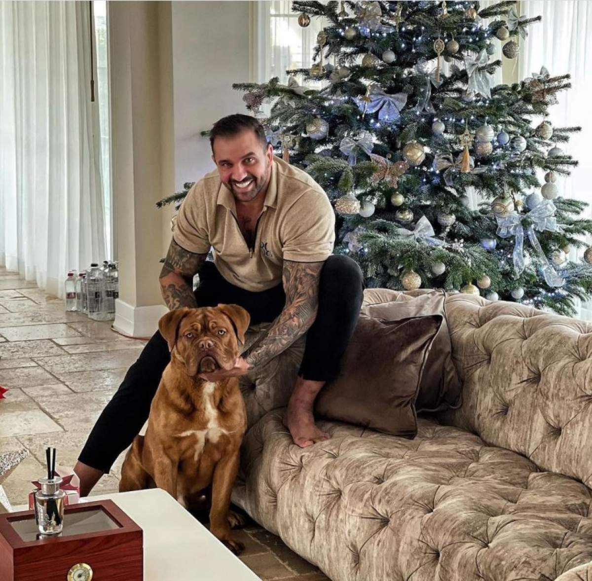 Alex Bodi este in living, sta pe marginea canapelei, se joaca cu cainele lui si zambeste