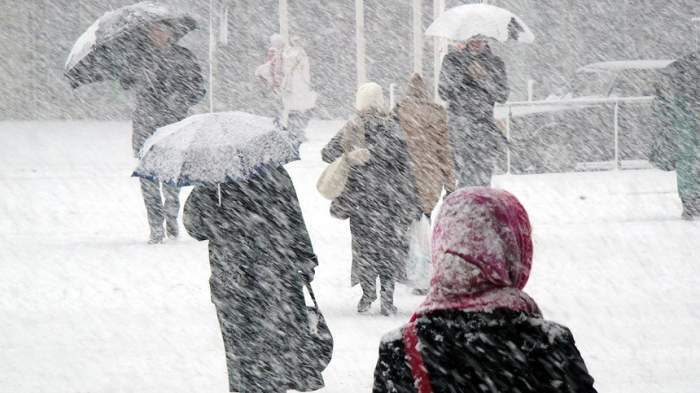 Imagine cu oameni care merg pe strada in timpul unei furtuni de zapada