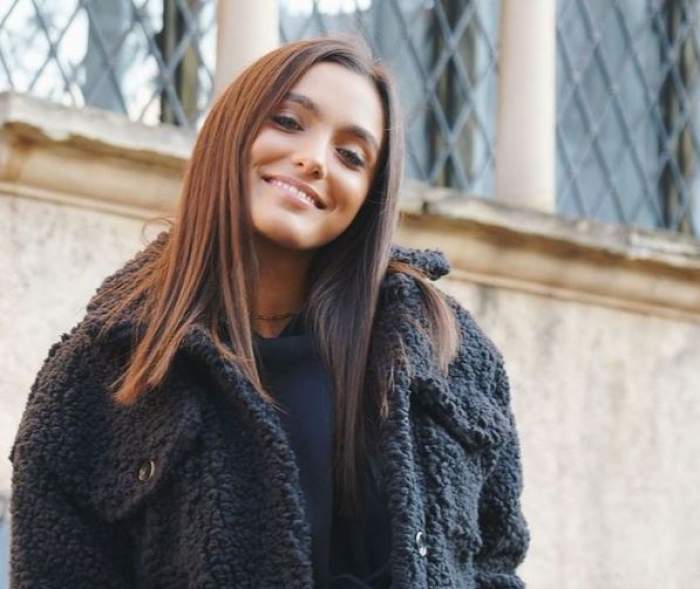 Alexia Eram se află afară. Vedeta zâmbește larg și poartă o haină de iarnă neagră.