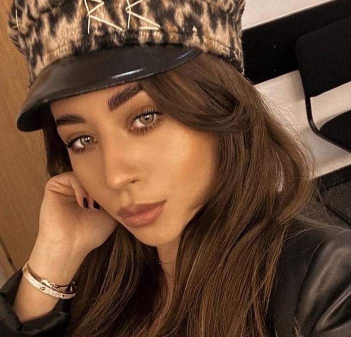 Nicole Cherry poartă o bască cu animal print pe cap. Artista e îmbrăcată cu o bluză din piele neagră.