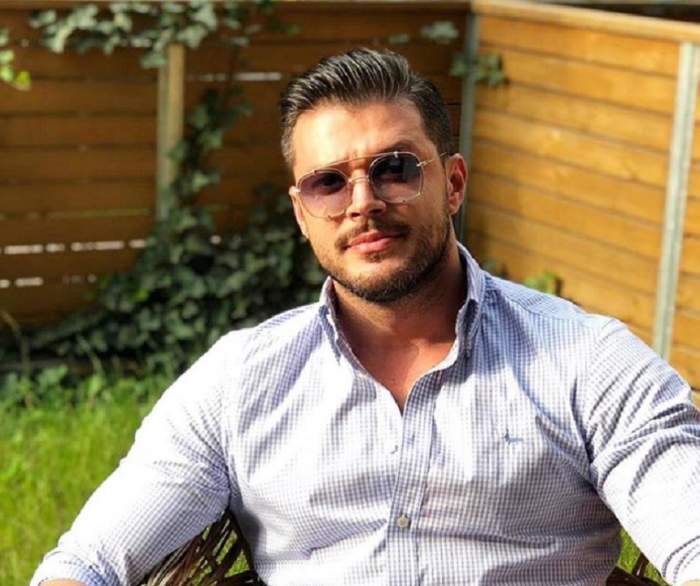Victor Slav, îmbrăcat în cămașă și purtând ochelari de soare, fotografiat stând pe scaun
