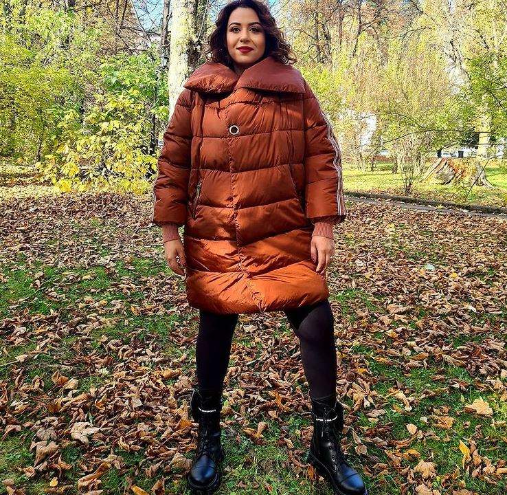 Oana Roman se află în parc. Vedeta poartă o geacă oversized, maro, și pantaloni negri, mulați.