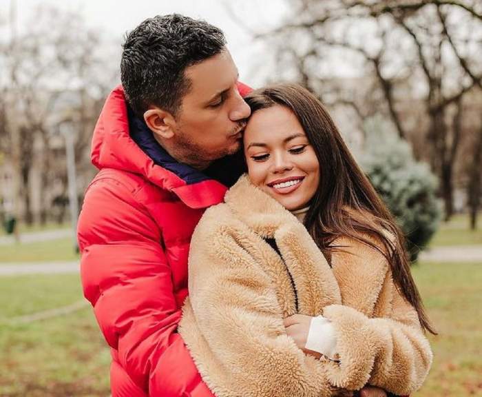 Denisa Hodișan și Flick se află în parc. El o îmbrățișează și o sărută pe frunte și poartă o geacă roșie, iar ea zâmbește larg și poartă o geacă de iarnă crem.