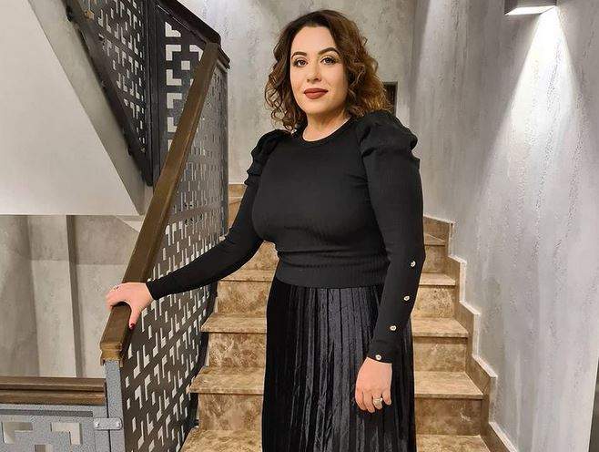 Oana Roman se află pe scări. Vedeta e îmbrăcată într-o bluză și o fustă neagră și se ține de balustradă.
