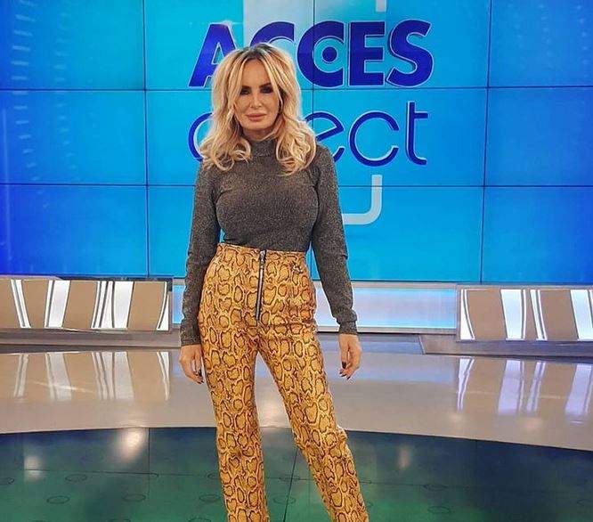 Daniela Gyorfi se află la Acces Direct. Vedeta poartă o maletă gri și niște pantaloni mulați, stil snake print.