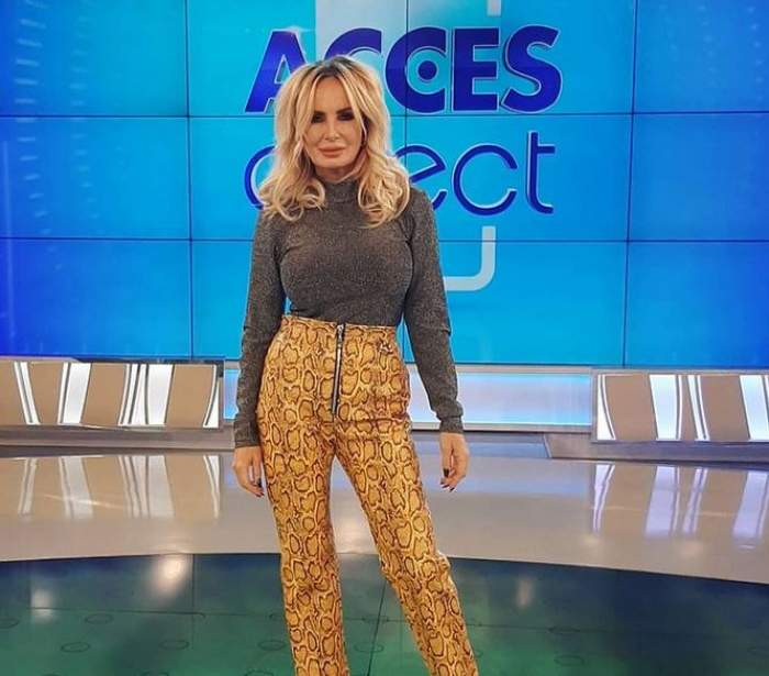 Daniela Gyorfi se află la Acces Direct. Vedeta poartă o maletă gri și niște pantaloni mulați, stil snake print.