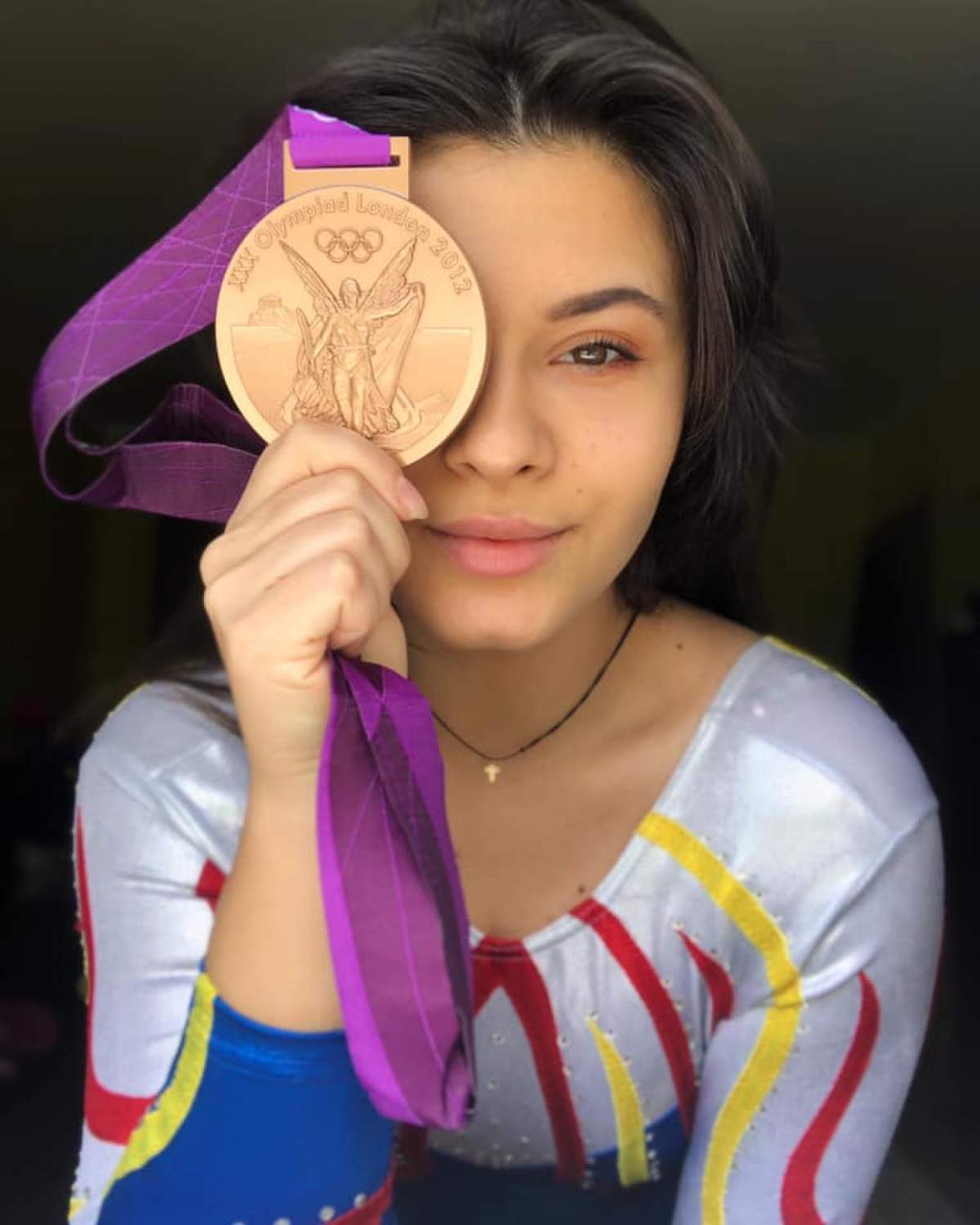 Diana Bulimar poarta costumul de gimnastica si isi acopera un ochi cu o medalie de aur